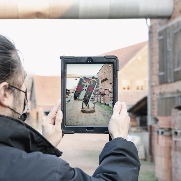Außengelände der Ziegelei mit Ipad auf dem eine AR-Skulptur zu sehen ist.
