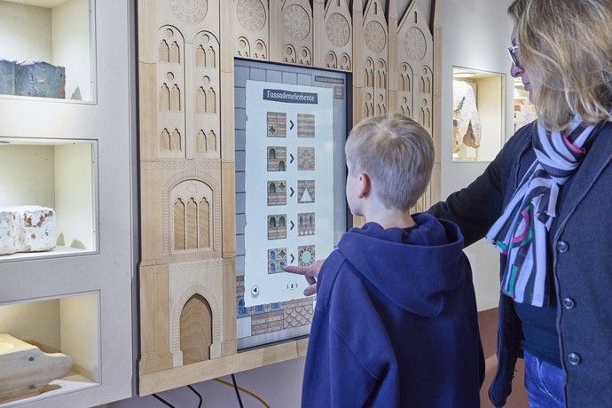 Junge und Frau stehen vor einem digitalem Screen in einer Holzfassade