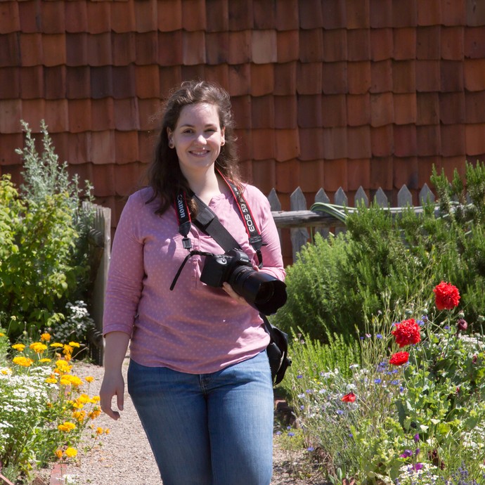Eine Frau steht mit ihrer Kamera im Arbeitergarten.