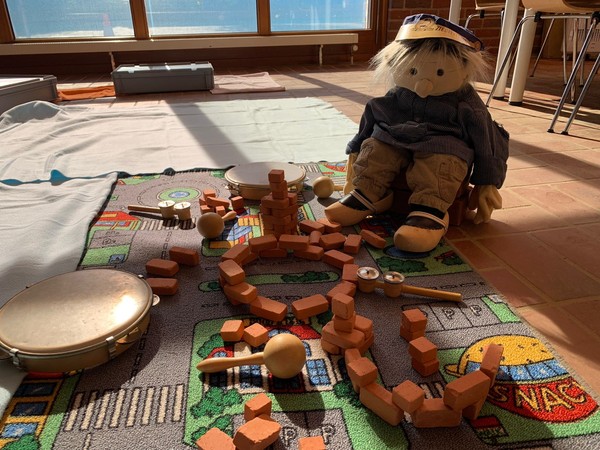 Kleine Tonziegel, Rhythmusinstrumente und eine Puppe auf einem Spielteppich.