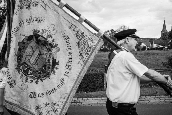Schwarz-Weiß-Foto: Ein Mann trägt die Fahne eines Zieglervereins beim Umzug. Foto: Veit Mette.