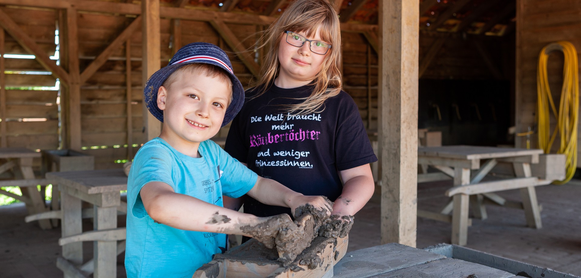 Ein Junge und ein Mädchen streichen Lehm in eine Ziegelform.