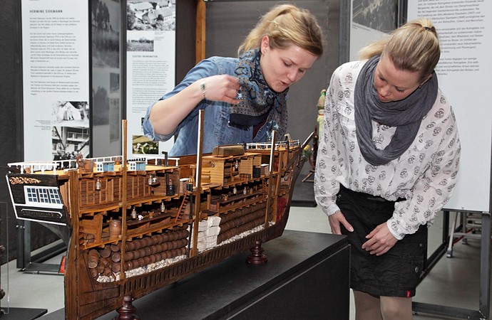 Zwei junge Frauen sehen sich ein Schiffsmodell aus Holz an.