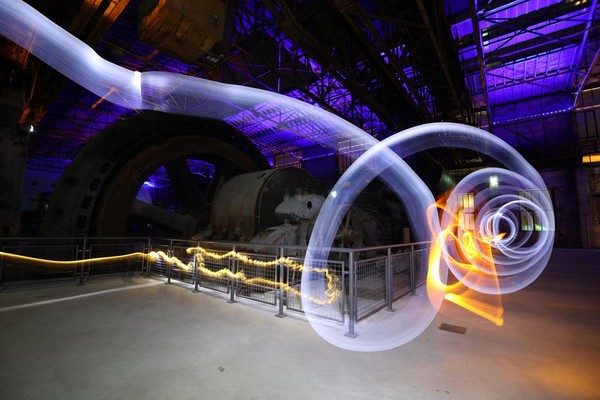 Ein gemalter Lichtstrahl vor einer Industriekulisse.