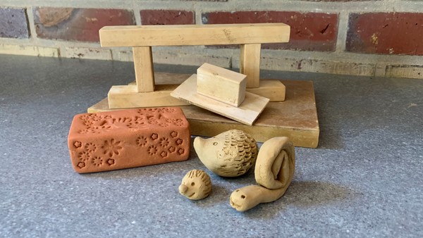 Ein verzierter Ziegel, ein Handstrichrahmen aus Holz und zwei Schnecken aus Ton.